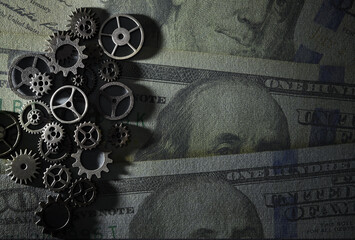 Assorted metal gears with hundred dollar bills background