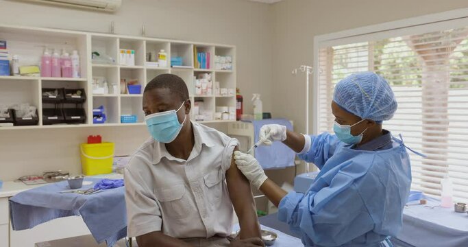Black African female doctor nurse gives a black african male patient the Covid-19 vaccine injection