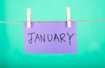  January word written on a Purple color sticky note hanging with a wire in a Cyan background.