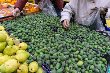 Heap of feijoa fruits in the supermarket for sale against the background of the hands of people choosing products