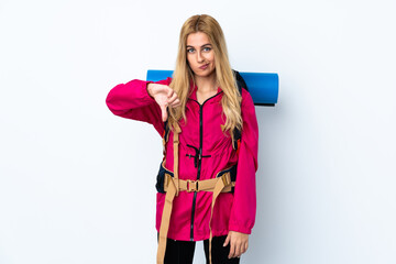 Young mountaineer woman with a big backpack over isolated white background showing thumb down sign