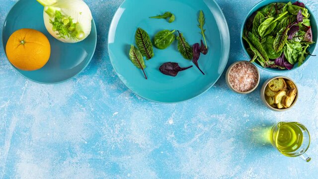 Making of salad with sliced fresh orange, fennel, lettuce, and crackers served on a blue plate on light blue table surface, top view. Ketogenic diet breakfast. Stop motion animation