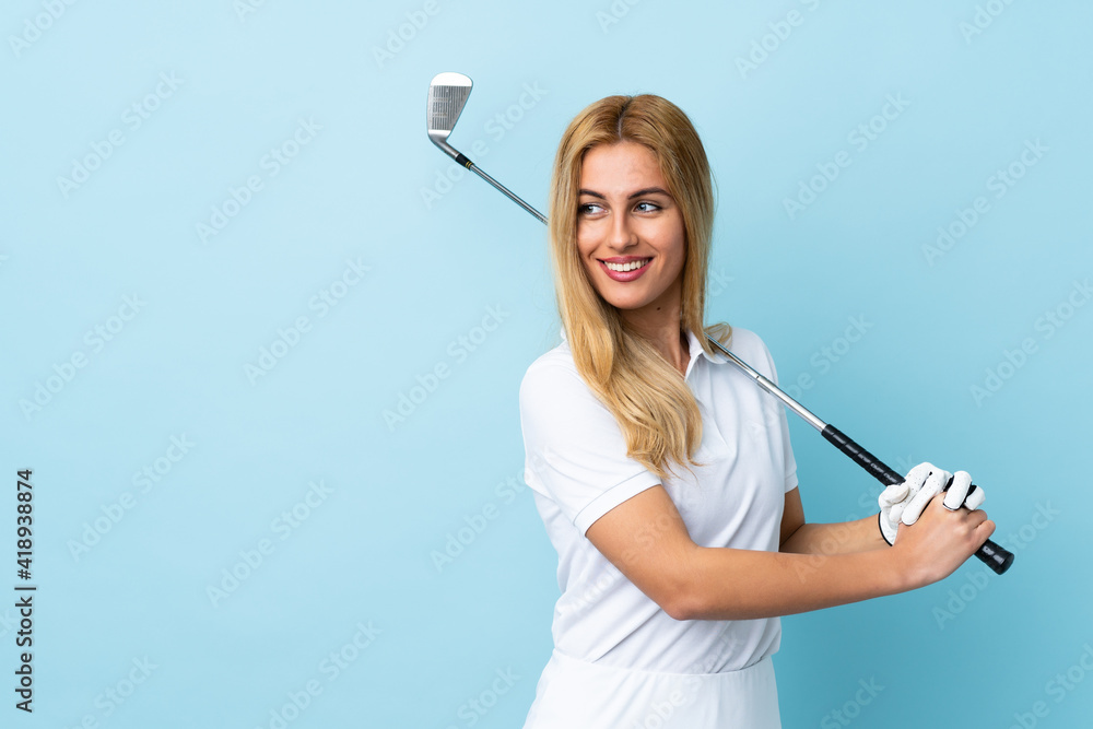 Wall mural Young Uruguayan blonde woman over isolated blue background playing golf