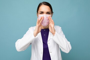 Young angry beautiful woman in reusable virus protective mask on face against coronavirus saying something negative isolated on the blue background wall