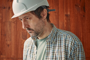 Portrait of concerned male worker with white protective helmet, employment and labor hardship...