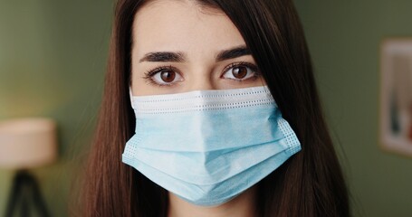 Close up of Caucasian beautiful young female enters the room and removing medical mask from face sitting down on couch at home with tired face. Quarantine coronavirus, healthcare concept