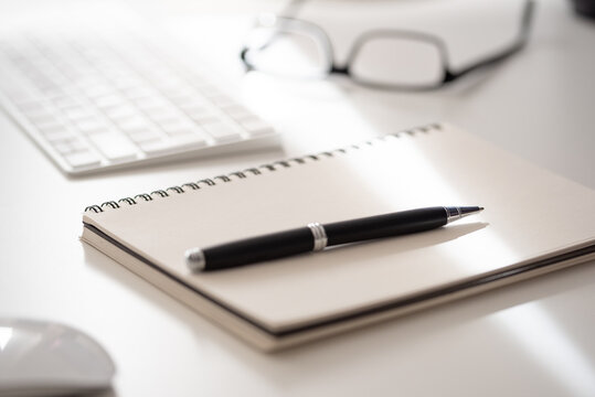 close-up of spiral notepad with ballpoint pen on white office desk, taking notes concept