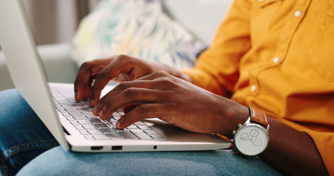 Close Up Shot Of African American Male Hands Typing On White Laptop Keyboard Sitting On Sofa In Room And Working. Man Fingers Tapping And Texting On Computer Browsing Online. Gadget Concept