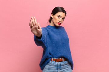 young pretty woman looking serious, stern, displeased and angry showing open palm making stop...