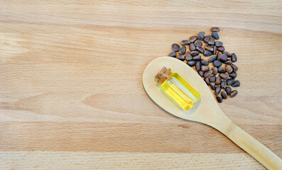 Essential cedar oil in small glass bottle and nuts in wooden spoon on wooden background. Copy space.