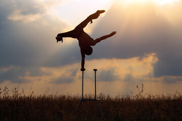 A man of athletic build performs complex gymnastic exercises in a field at sunset.