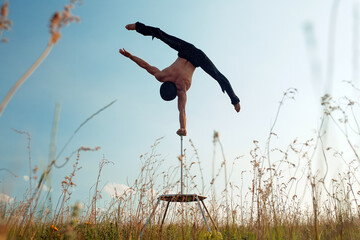 A man of athletic build performs complex gymnastic exercises in a field at sunset.