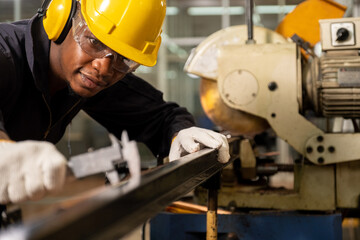 Professional African American engineer or worker wearing a hard hat and using vernier for measuring the piece of metal pipe and smiling in the factory.