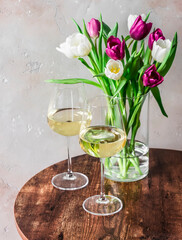 Bouquet of colorful tulips and two glasses of white wine on a wooden table