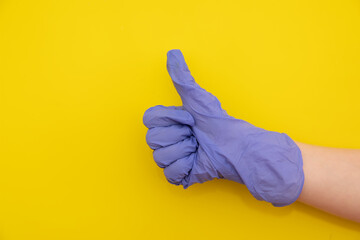 Girl showing thumbs up in a medical glove against yellow background