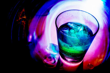 A glass of green drink with ice on a glass table on the vibrant neon colors background.
