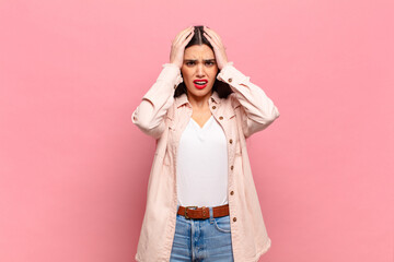 young pretty woman feeling horrified and shocked, raising hands to head and panicking at a mistake