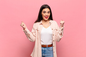 young pretty woman feeling happy, positive and successful, celebrating victory, achievements or...