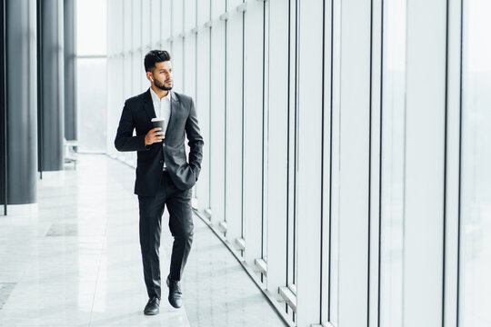 A Modern Bearded Indian Man Walks Down The Corridor Of A Modern Building, A Busy Businessman Goes To A Business Meeting