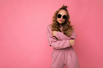 Photo shot of beautiful positive young dark blonde woman wearing casual clothes and stylish sunglasses isolated over colorful background looking at camera