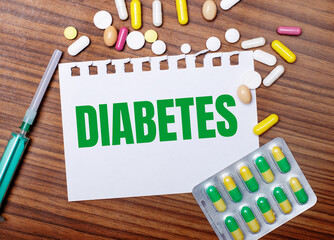 On a wooden table, a syringe, pills and a sheet of paper with the inscription DIABETES. Medical...