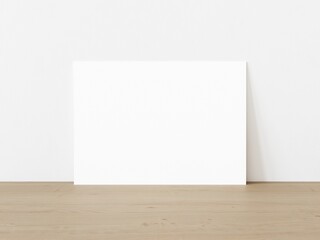 Blank horizontally oriented rectangular poster standing on wooden floor leaning on white wall. 3D Illustration