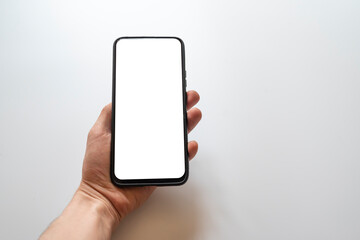 Hand holding black smartphone mockup blank screen isolated on white background. Touch screen mobile phone put in a vertical position. This photo can be used for communication or technology concept.