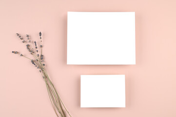 Two blank white paper card on pink pastel surface with lavender flower. Mock-up of horizontal blank greeting cards. Minimal business brand template. Flat lay, top view