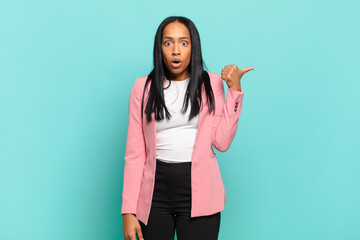young black woman looking astonished in disbelief, pointing at object on the side and saying wow,...