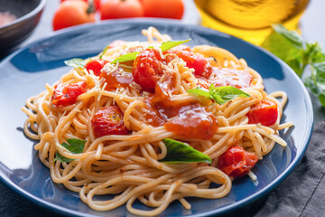 Tasty appetizing classic italian spaghetti pasta with tomato sauce, cheese parmesan and basil on plate and ingredients for cooking pasta on dark table.