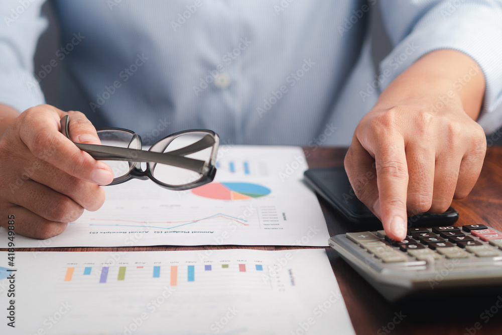 Poster close-up of hand holding a glasses reviewing the chart, graph report and calculating on the calculat
