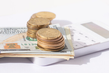 A calculator,stacks of coins and a bundle of 100 dollars on a white background