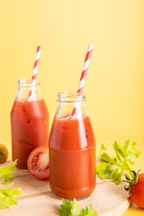 glass bottle of tomato juice, lime with fresh bright bunch of tomatoes isolated on green background, green parsley. vegetable drink.