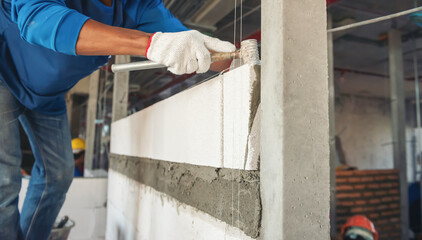 Construction worker man in uniform and safety equipment have job on building. Installing brick wall on site. 