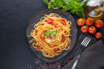 Tasty appetizing classic italian spaghetti pasta with tomato sauce, cheese parmesan and basil on plate  and ingredients for cooking pasta on dark table. Flat lay top view copy spce..