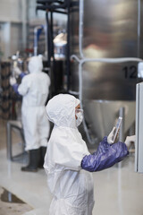 Vertical side view portrait of female worker wearing protective suit while operating equipment at chemical plant