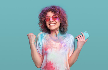 Excited woman with smartphone enjoying Holi festival