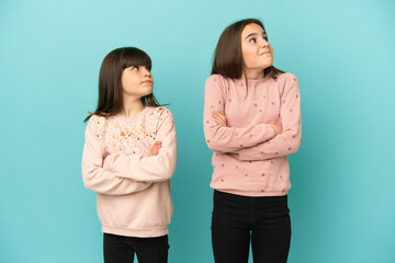 Little sisters girls isolated on blue background making doubts gesture while lifting the shoulders