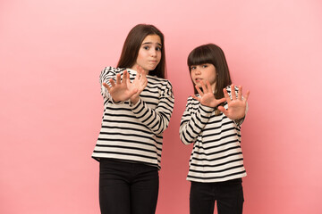 Little sisters girls isolated on pink background is a little bit nervous and scared stretching hands to the front