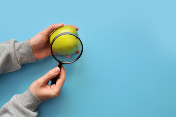 A person examines an apple through a magnifying glass and checks whether it is clean enough