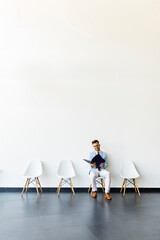 Young man sitting in the waiting room with a folder in hand before an interview
