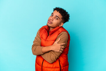 Young african american curly man isolated on blue hugs, smiling carefree and happy.