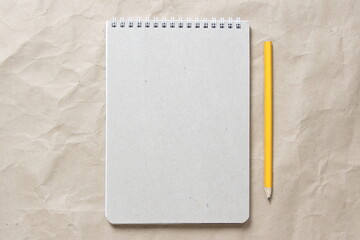 Gray notepad with white coiled spring and pencil on a background of beige crumpled craft paper. With empty space for text and design