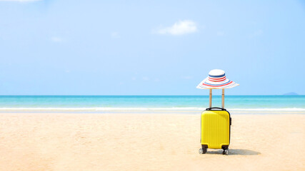 Travel on Summer and tourist planning with yellow suitcase with fashion hat fashion in the beautiful beach. Travel in holiday. Blue sky and sand background, on travel in summer concept.