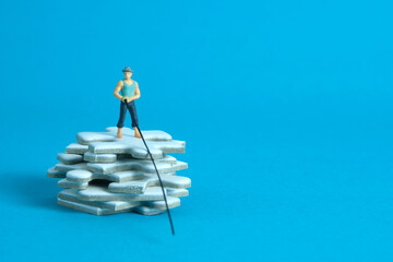 Miniature toy photography people. Fisher standing above white puzzle jigsaw stack. Isolated on blue background.