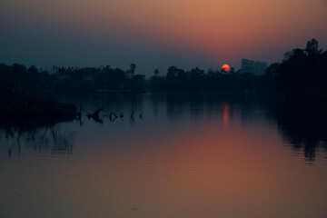 Naklejka premium A beautiful sunset at Rabindra Sarobar Lake in Kolkata, with reflection of golden looking sun in lake water.