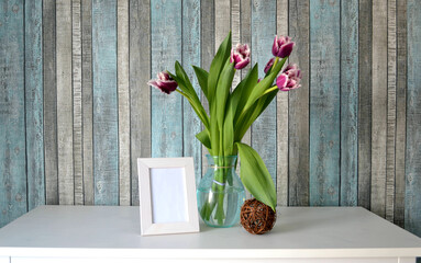 Spring still life with bouquet of lilac fringed tulips in glass bowl and blank white wooden frame...