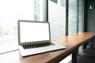 Laptop with blank screen on wooden table in front of office window - technology concept