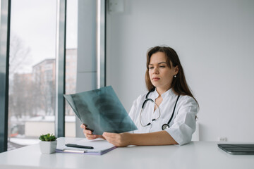 Young caucasian woman doctor wearing white medical coat and stethoscope holds the x-ray