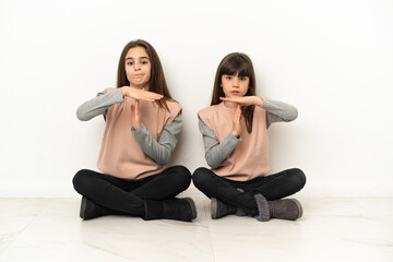 Little sisters sitting on the floor isolated on white background making stop gesture with her hand to stop an act